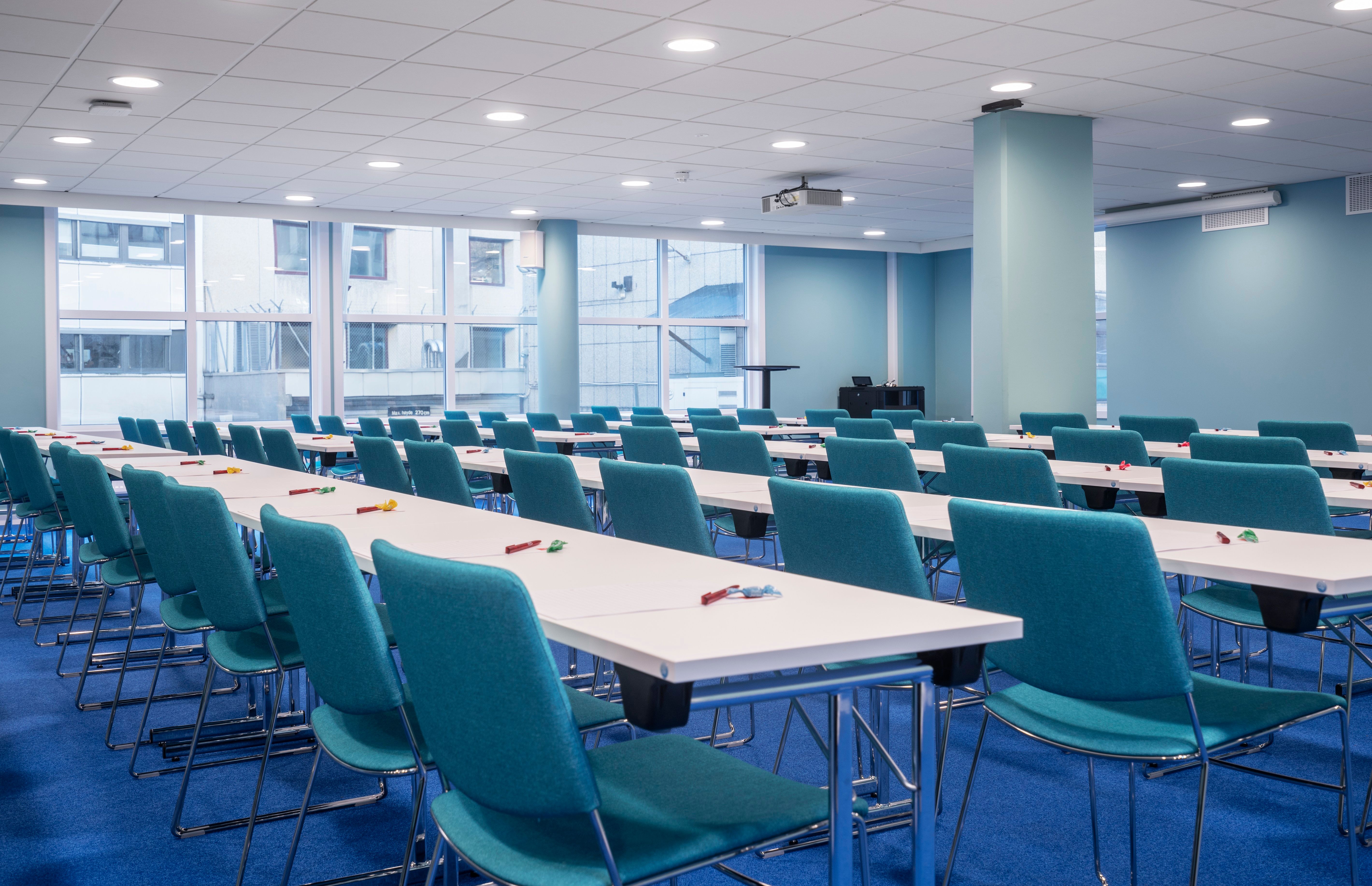 Meeting room with blue chairs and floor, white tables. Classroom seating. Large windows. Thon Hotel Slottsparken, Oslo. Photo