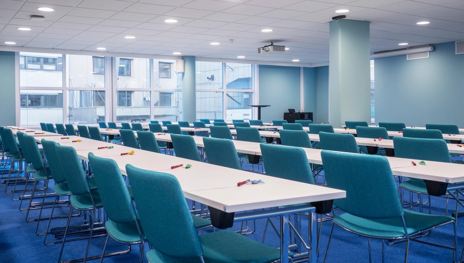 Meeting room with blue chairs and floor, white tables. Classroom seating. Large windows. Thon Hotel Slottsparken, Oslo. Photo