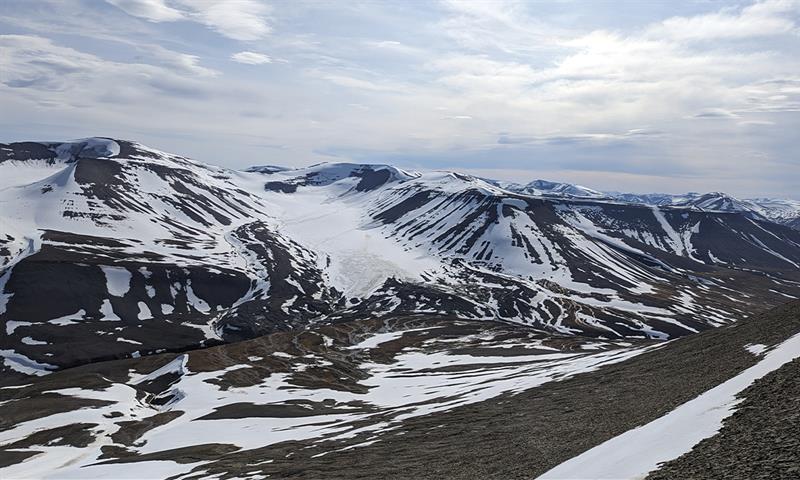 A lightly snow-covered mountain landscape with a glacier and a cloudy sky in the background