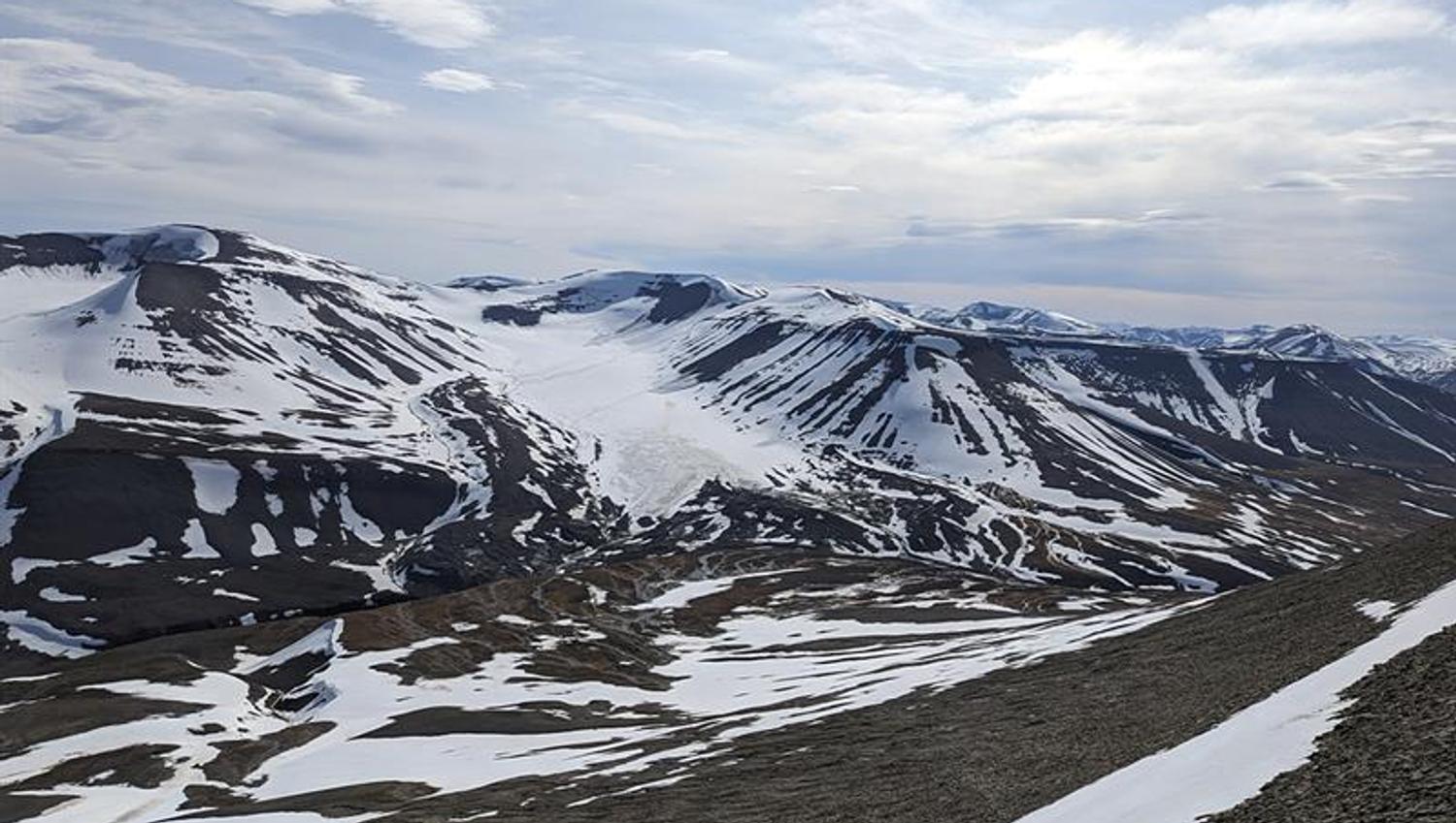 A lightly snow-covered mountain landscape with a glacier and a cloudy sky in the background