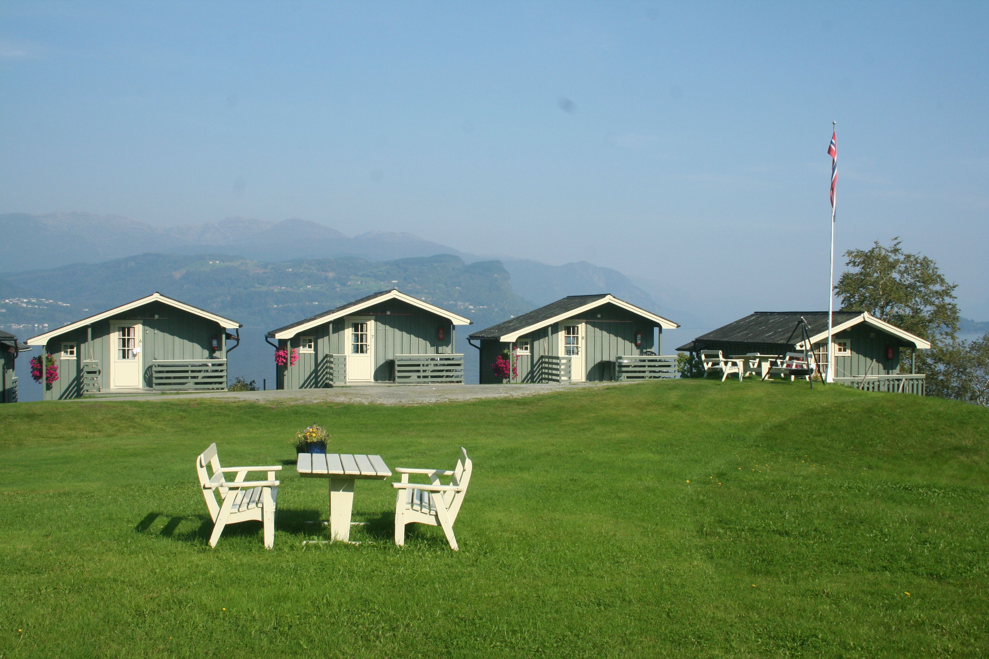 Green outdoor area with seating and fjord views over the cabins at Oddland Camping.