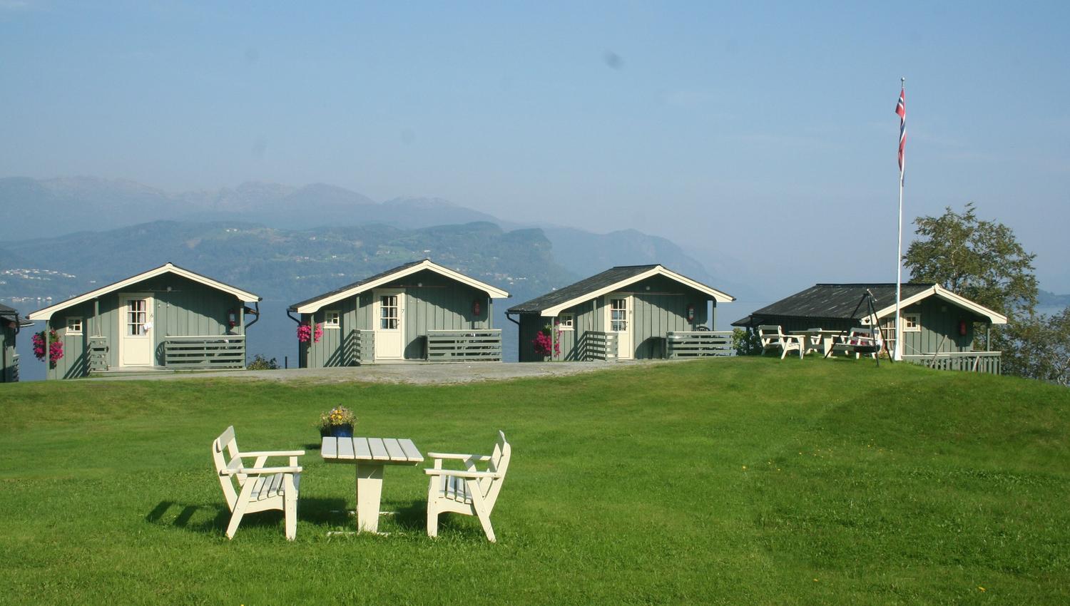 Green outdoor area with seating and fjord views over the cabins at Oddland Camping.