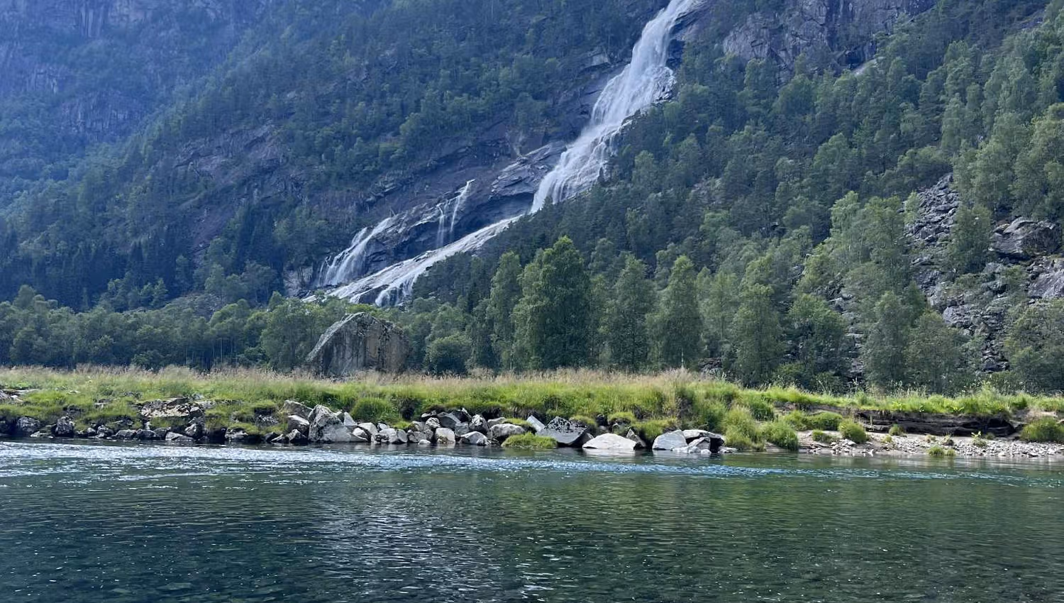 Zelte und Wohnmobile auf den grünen Wiesen des Hildal Camping mit dem Wasserfall im Hintergrund.