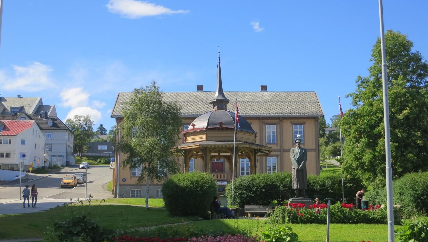 Historic building with a dome and front garden, statue and flower beds in the foreground.