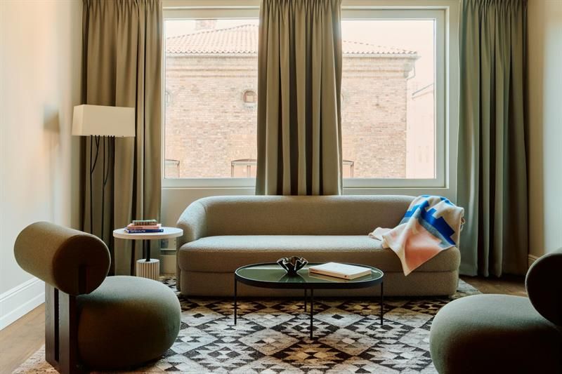 The living area is furnished with a sofa, armchairs and a coffee table. Large windows provide natural daylight.