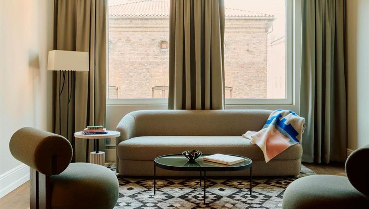 The living area is furnished with a sofa, armchairs and a coffee table. Large windows provide natural daylight.