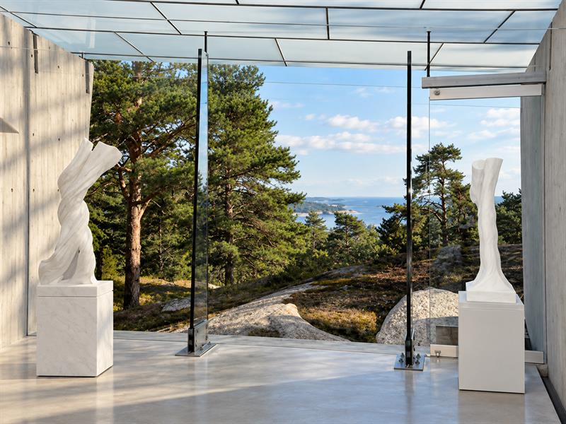 Hvite marmorskulpturer i Midtåsen Skulpturpaviljong med store glassflater og utsikt mot furutrær og Sandefjordsfjorden.
