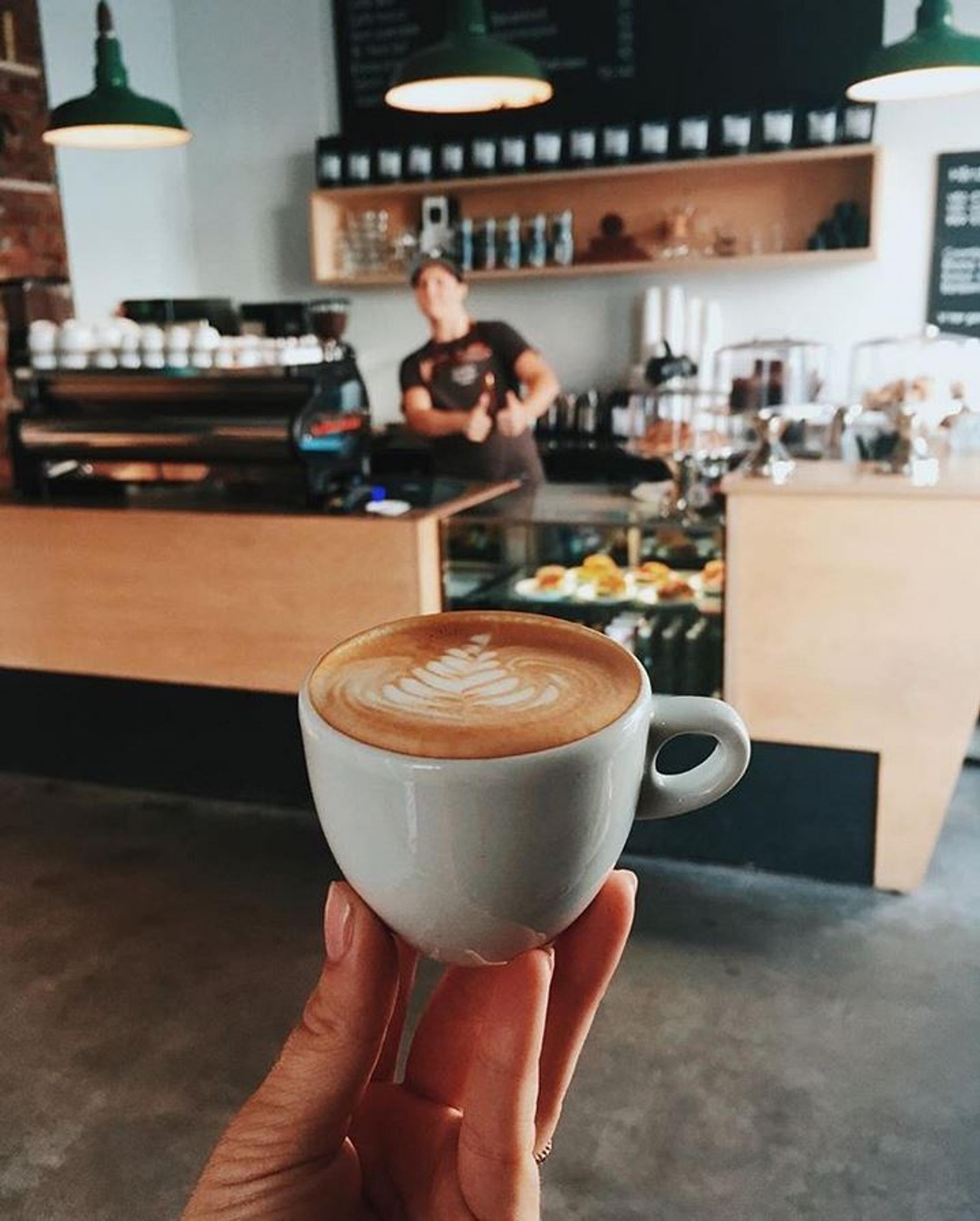 a hand holding up a coffee with the coffee shop in the background