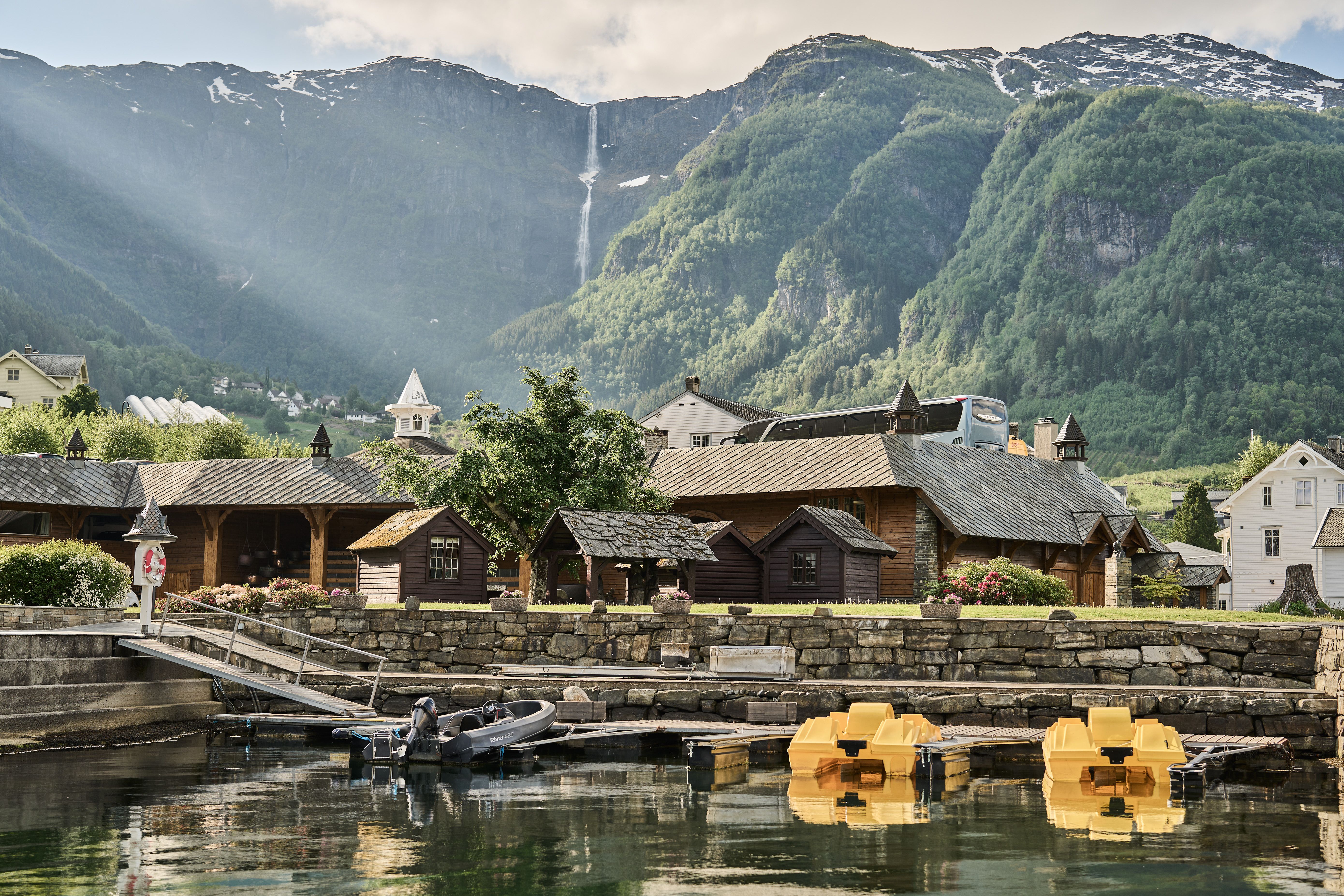 View of the boathouse and cabins at Hotel Ullensvang, with mountains in the background.