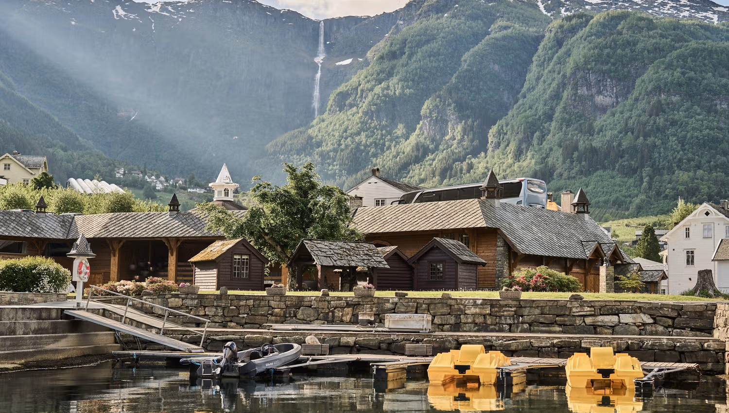 View of the boathouse and cabins at Hotel Ullensvang, with mountains in the background.