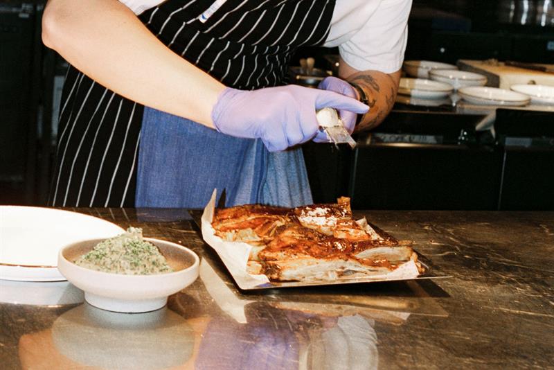 A chef plates meat at a kitchen counter under warm lights in an open restaurant kitchen.