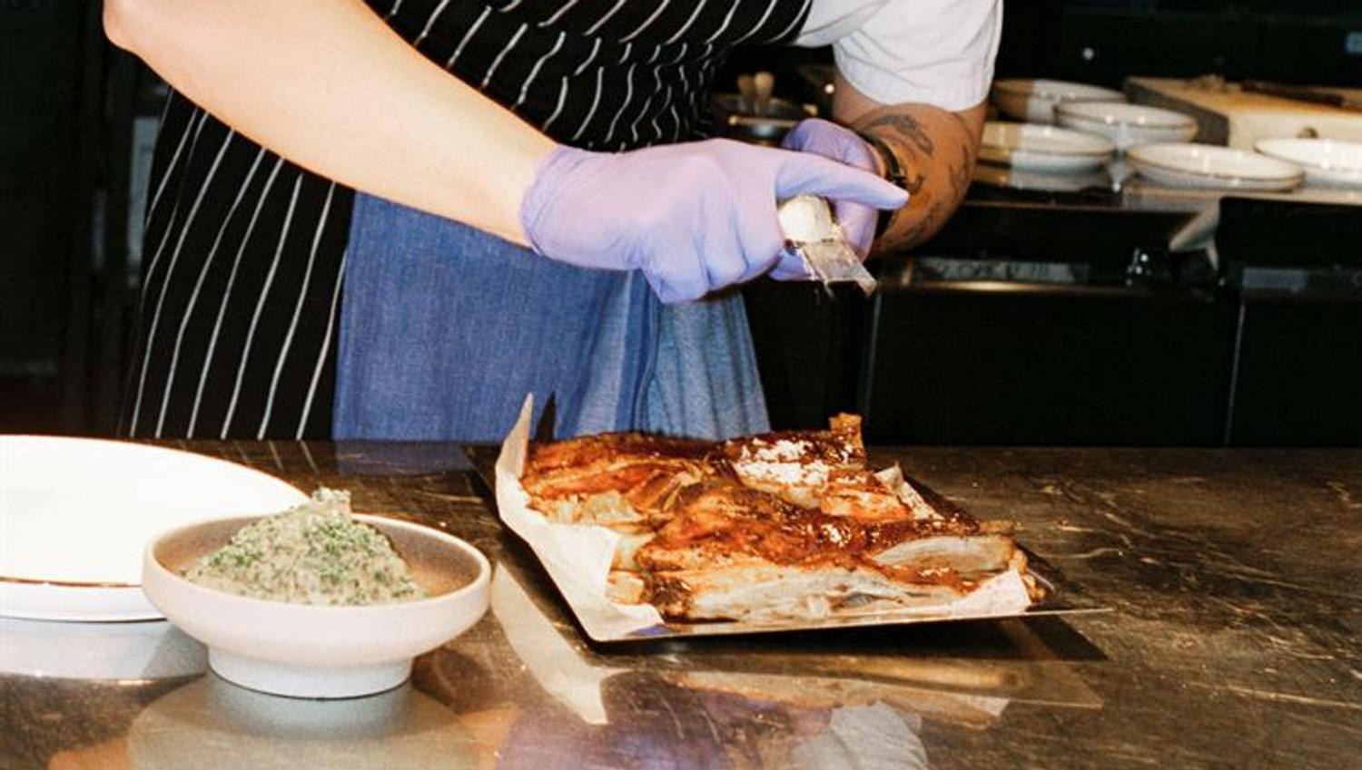 A chef plates meat at a kitchen counter under warm lights in an open restaurant kitchen.