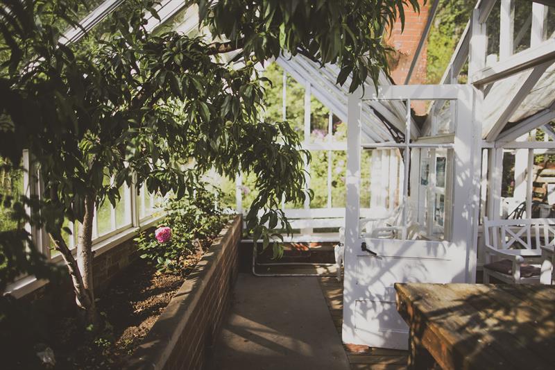 Inni drivhuset, blomsterbed på venstre side med planter, og hvit dør ut av drivhuset
