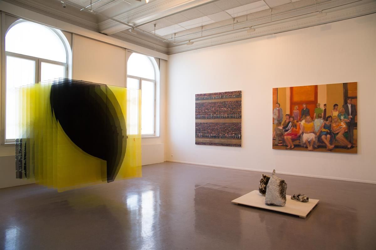 Art installation featuring hanging yellow threads with paintings in the background.
