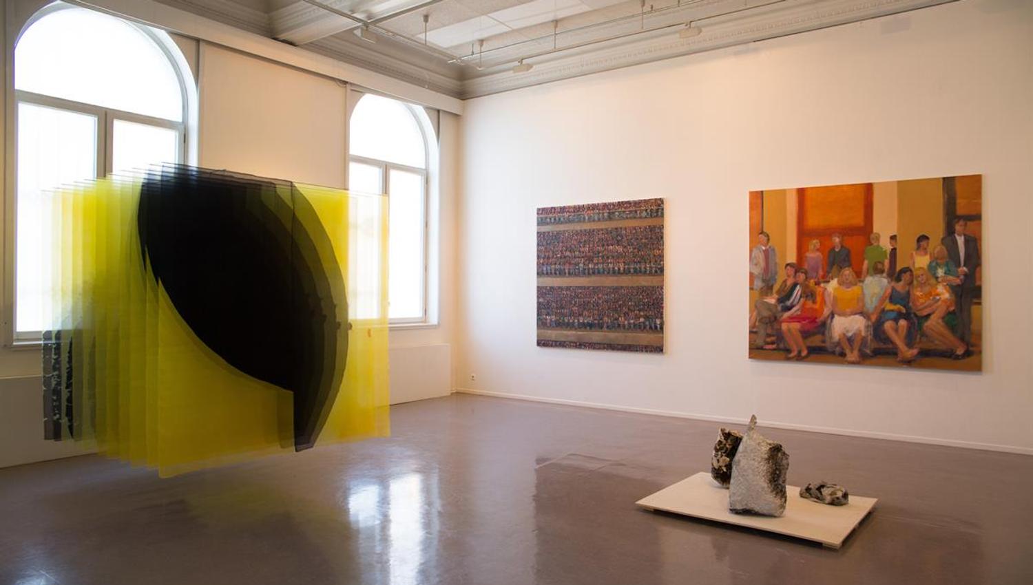 Art installation featuring hanging yellow threads with paintings in the background.