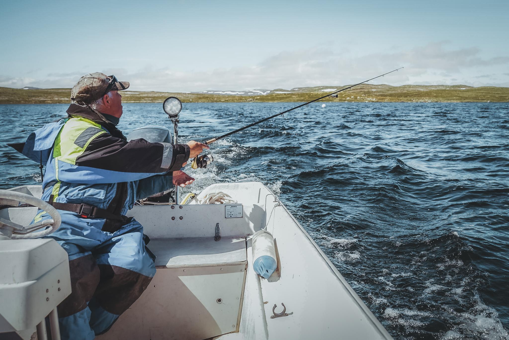 A man is fishing from a boat at the Halnefjord lake in the Hardangervidda.