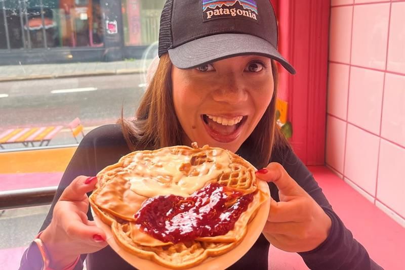A girl holding a waffle with sour cream and jam on it