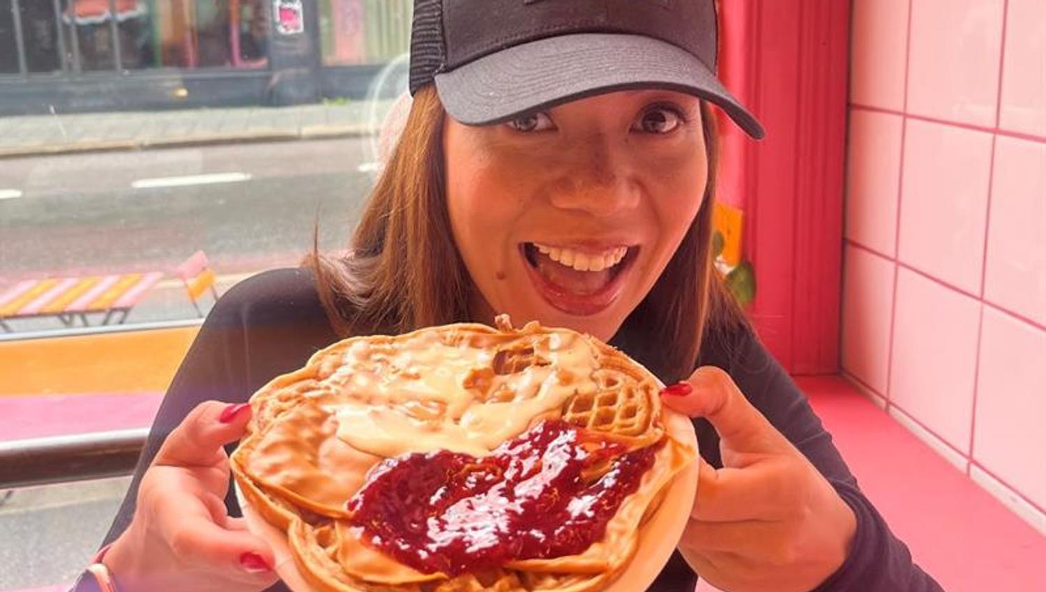 A girl holding a waffle with sour cream and jam on it