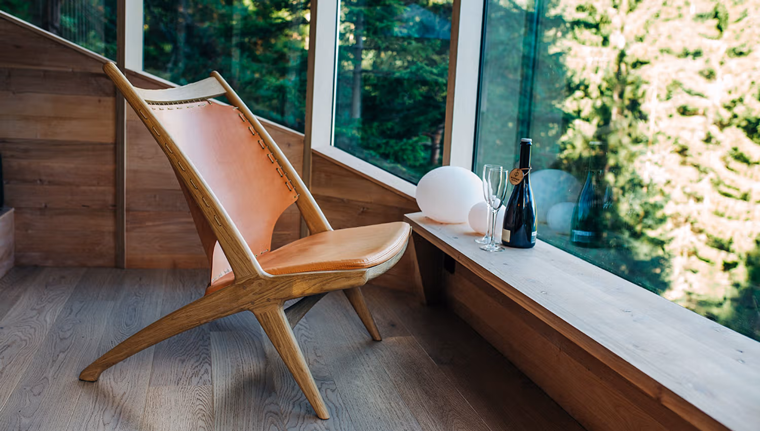 Komfortabelt sitteområde i Woodnest tretopphytte med store vindauge og utsikt til naturen utanfor.