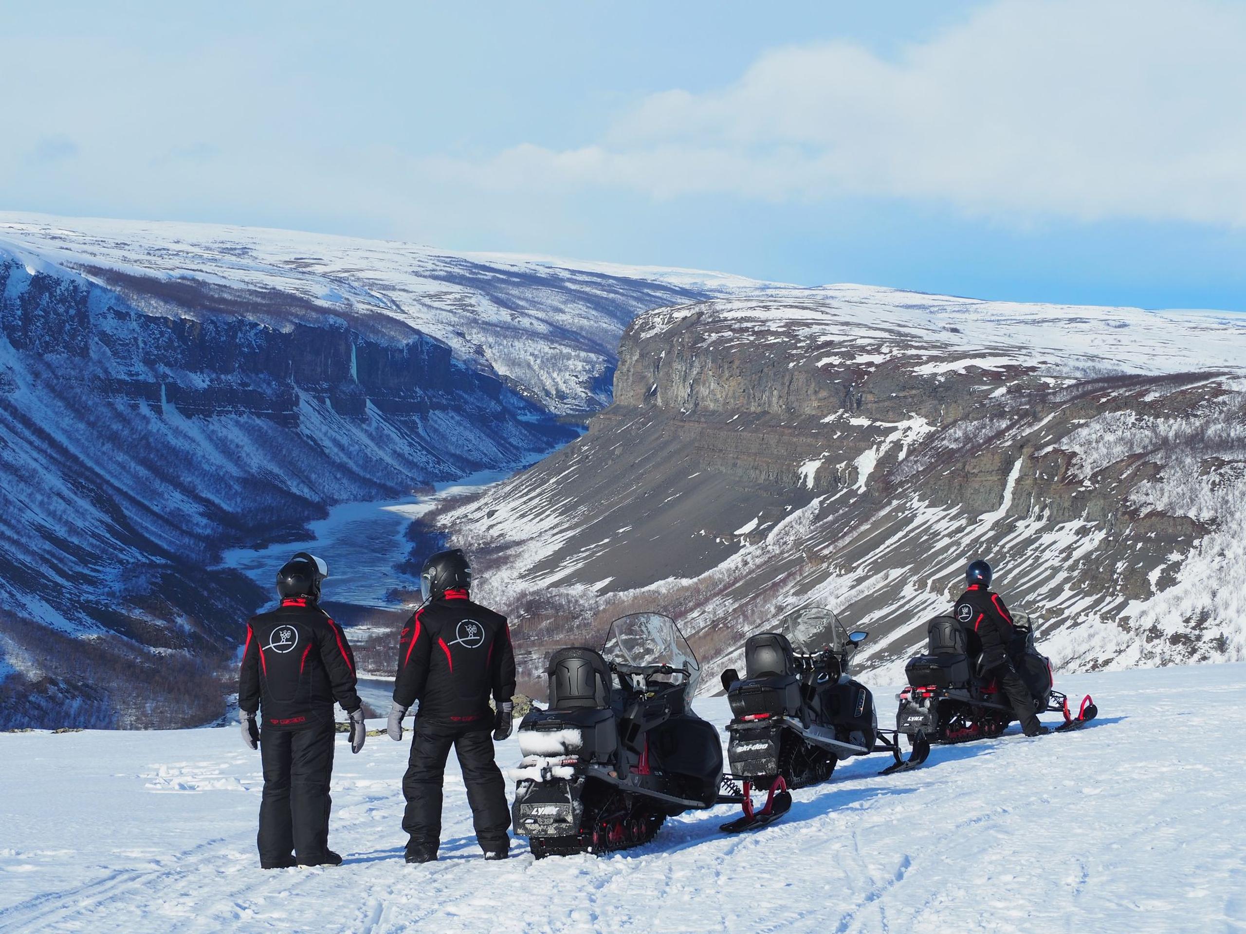 Trois personnes en tenue de neige admirent un paysage montagneux enneigé.