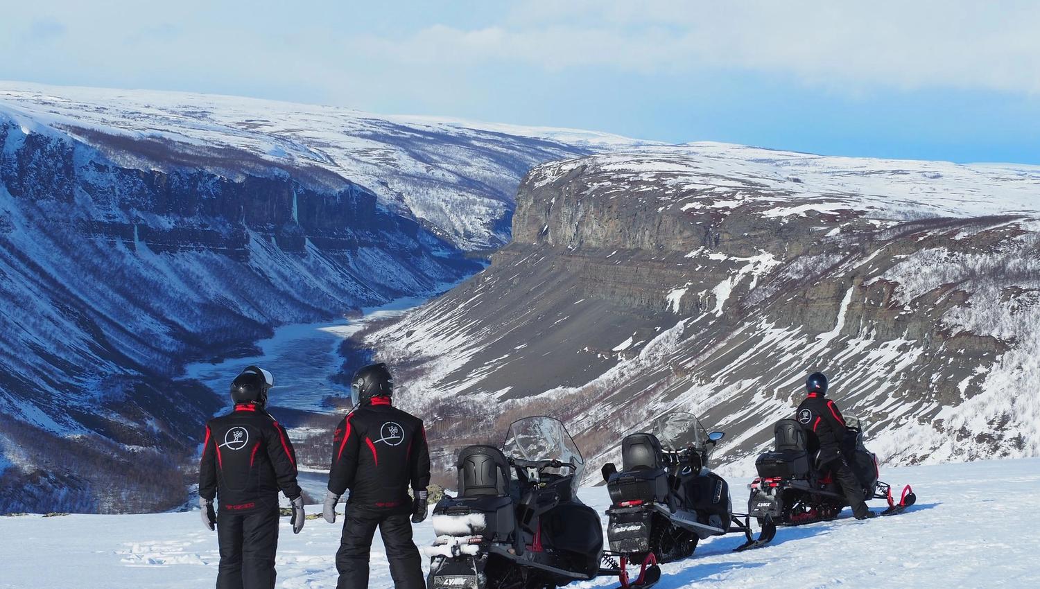 Trois personnes en tenue de neige admirent un paysage montagneux enneigé.