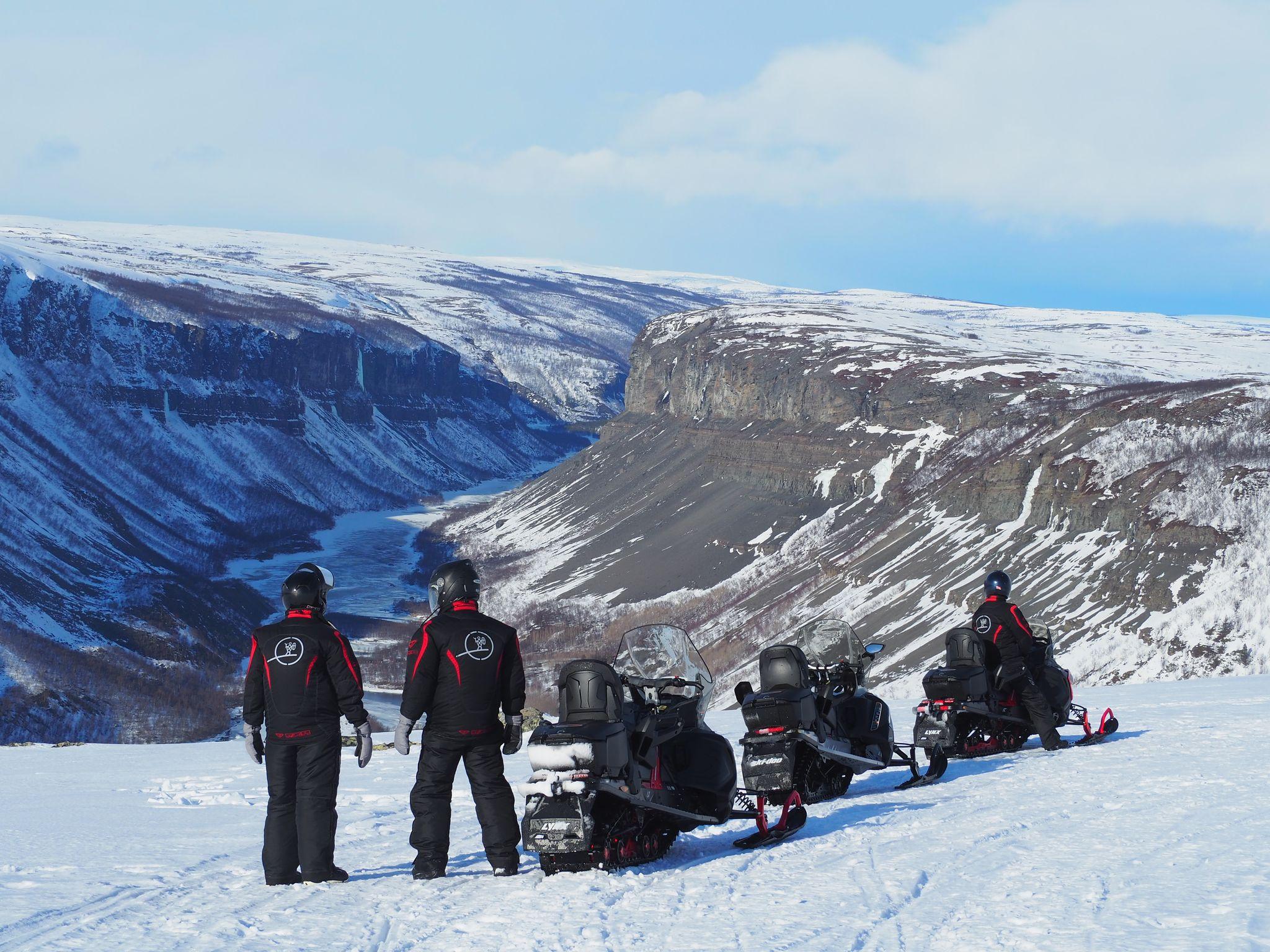 Trois personnes en tenue de neige admirent un paysage montagneux enneigé.