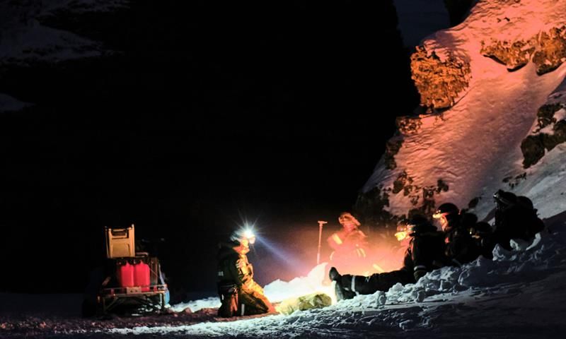 People are sitting on the ground next to a stony cliff. Mountian in the background. Clear starsky.