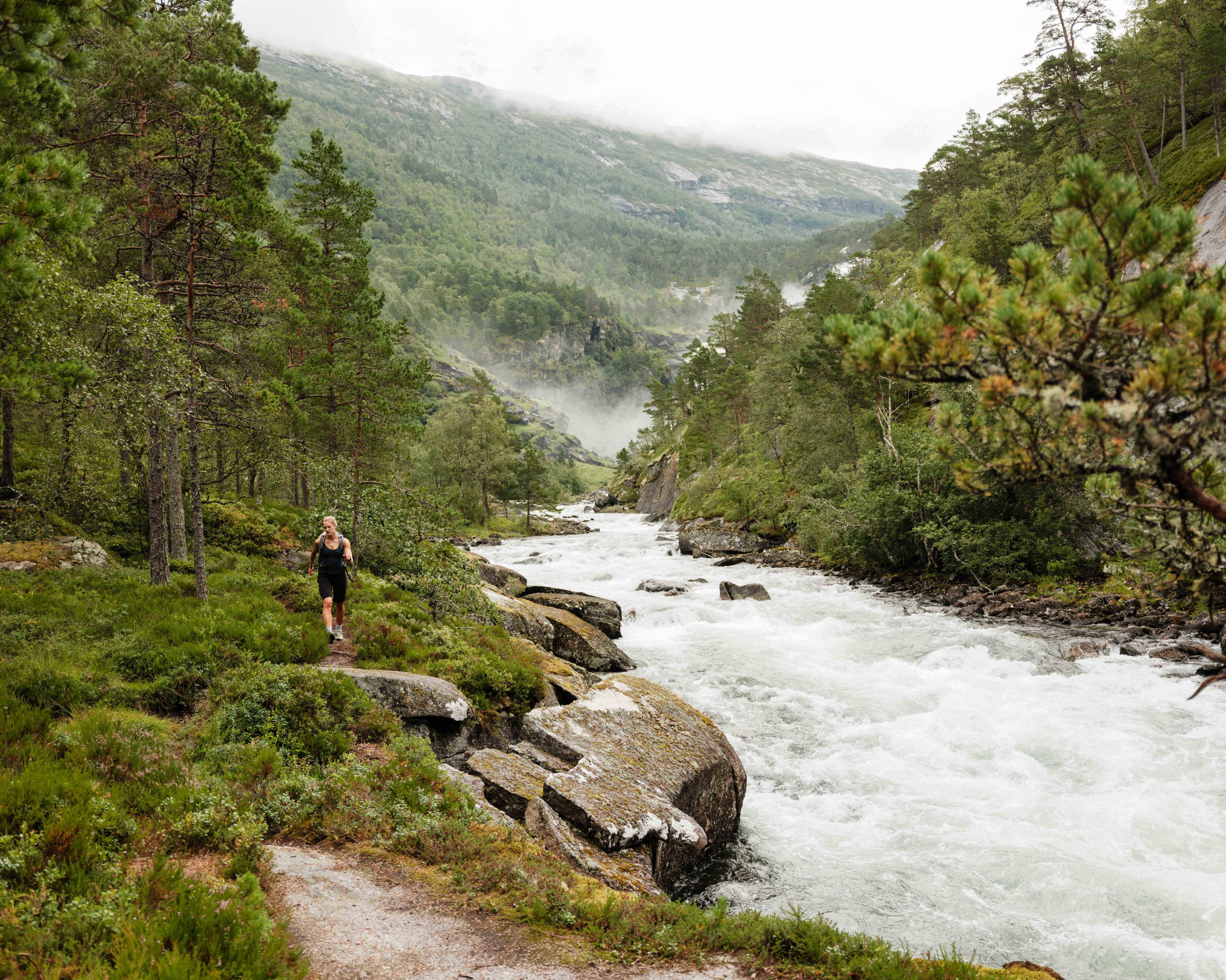 Hiking along the river in Husedalen, surrounded by lush forest and mist from the waterfalls.