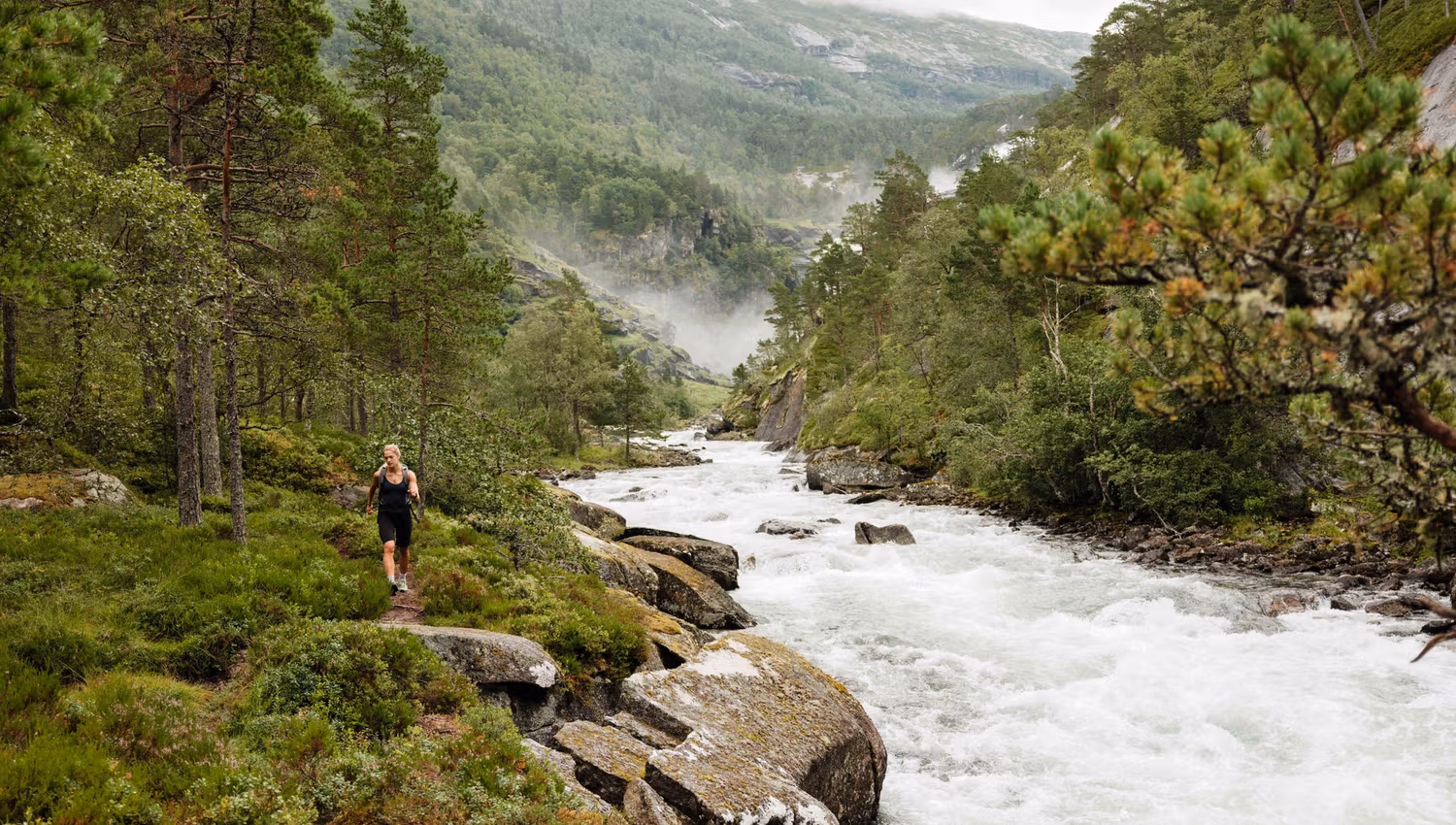 Hiking along the river in Husedalen, surrounded by lush forest and mist from the waterfalls.