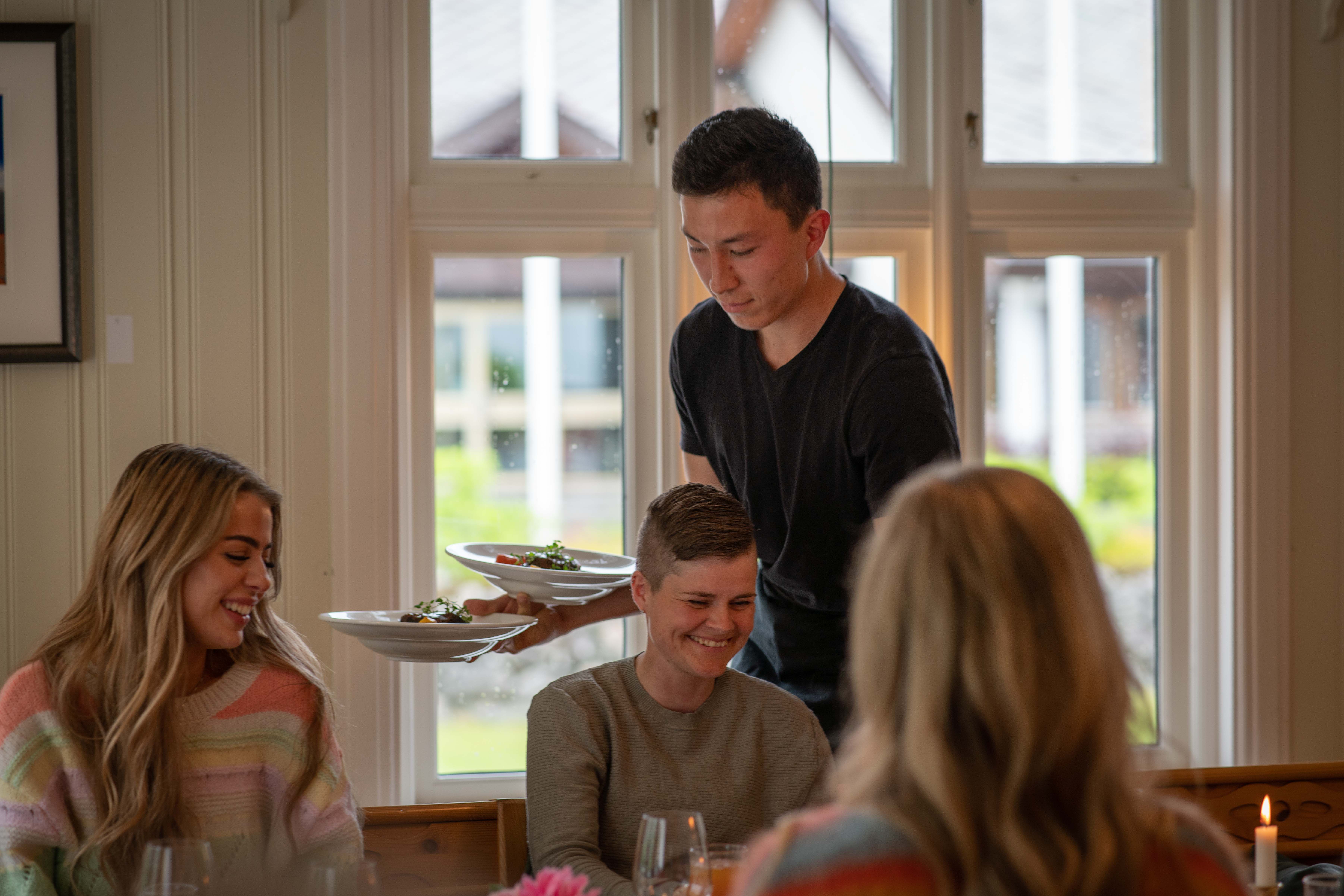 A waiter serving food to some female guests.