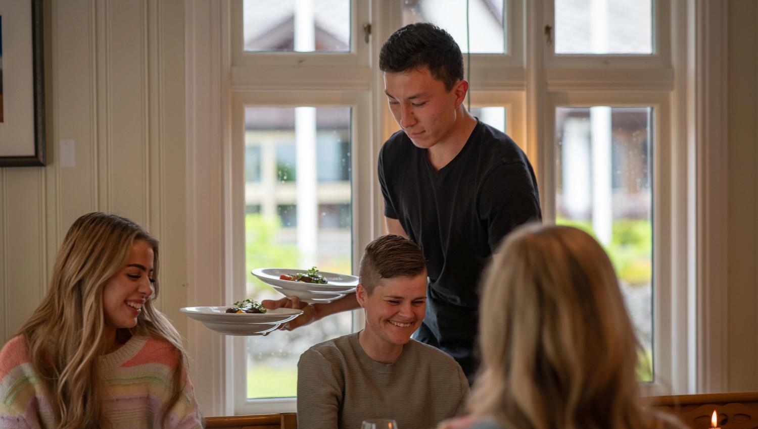 A waiter serving food to some female guests.