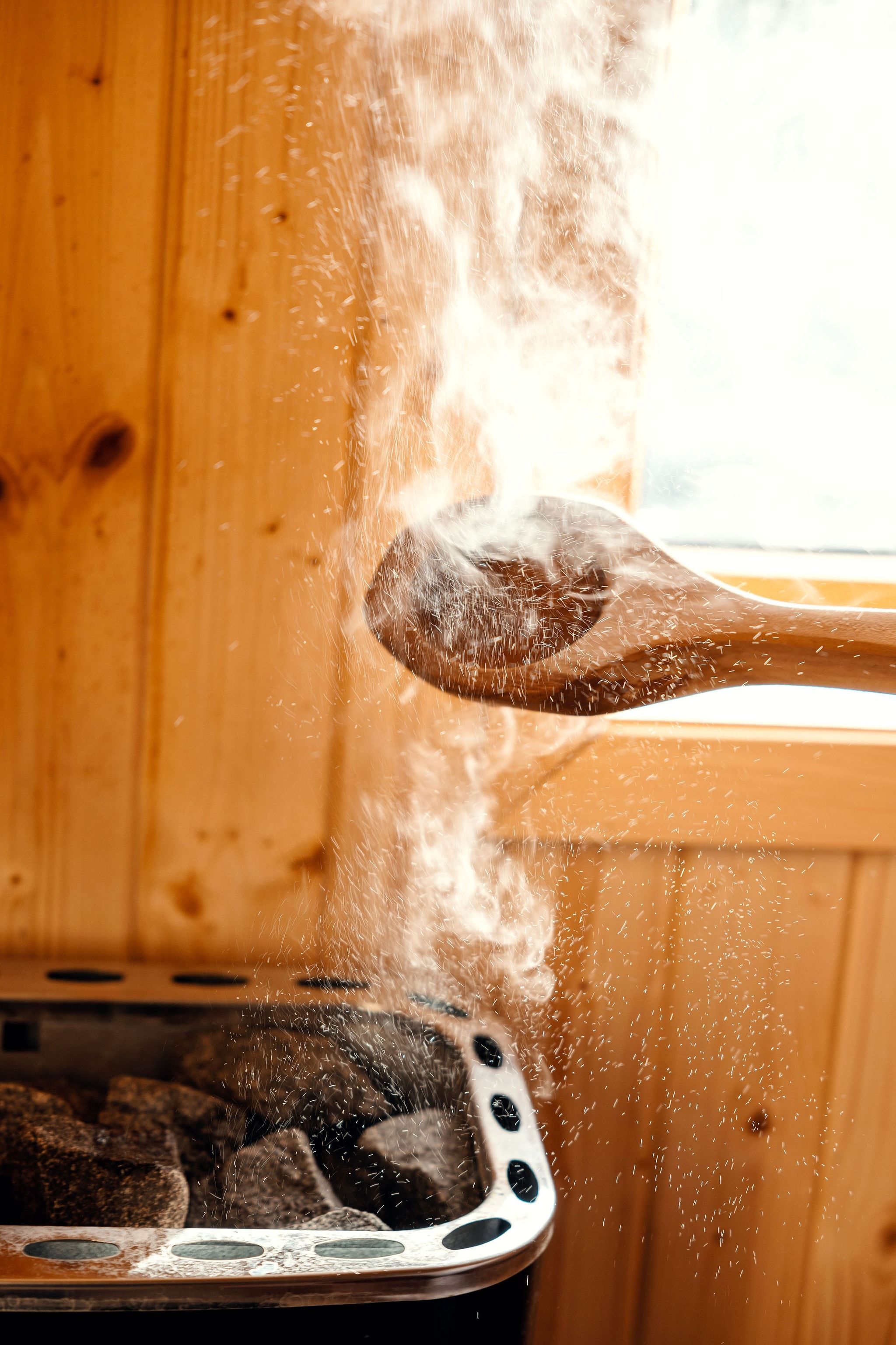 Water splashes onto hot sauna stones from a wooden ladle, sending a cloud of steam in a wood-paneled room at the Seahouse at Hornelen Panorama in Bremanger..