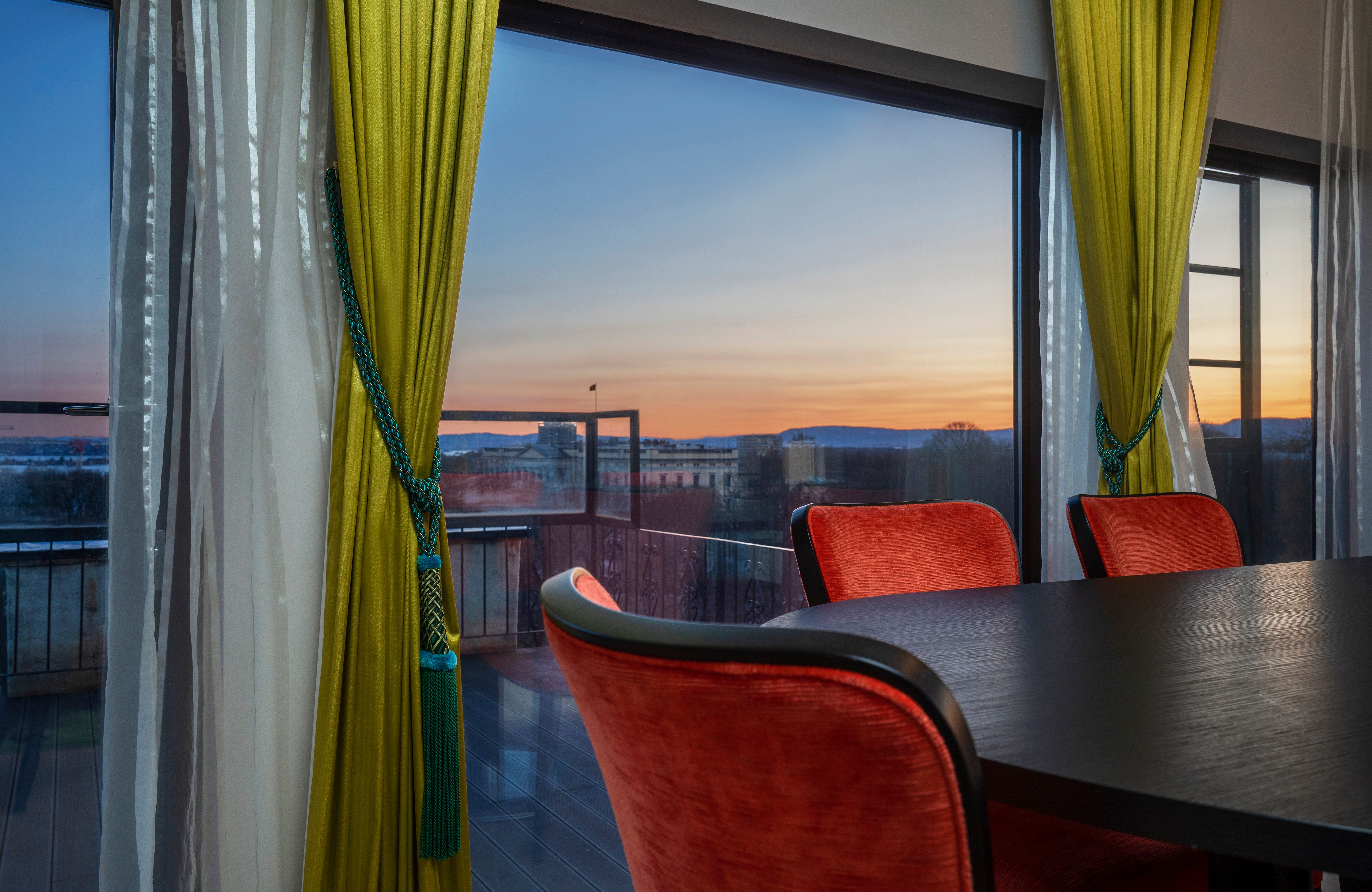 Meeting room with dark table. Red chairs in front of a panorama window. Evening view. Thon Hotel Slottsparken, Oslo. Photo