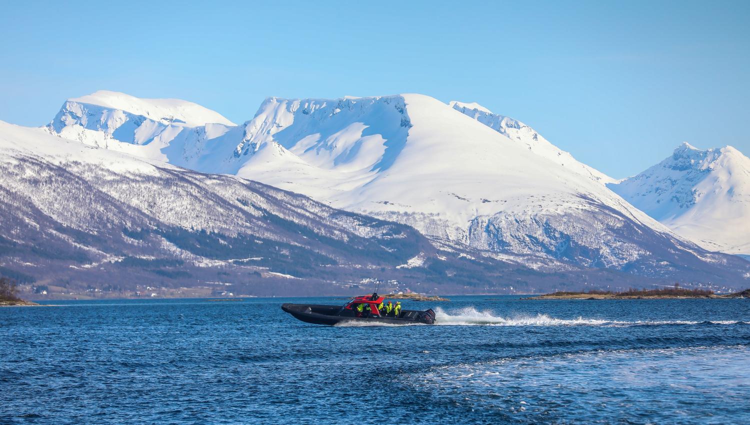 RIB båt kjører fort med snødekte fjell i bakgrunnen