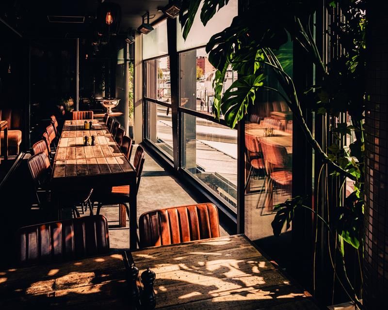 Long tables positioned alongside windows overlooking the street. The space accommodates both small and larger groups.