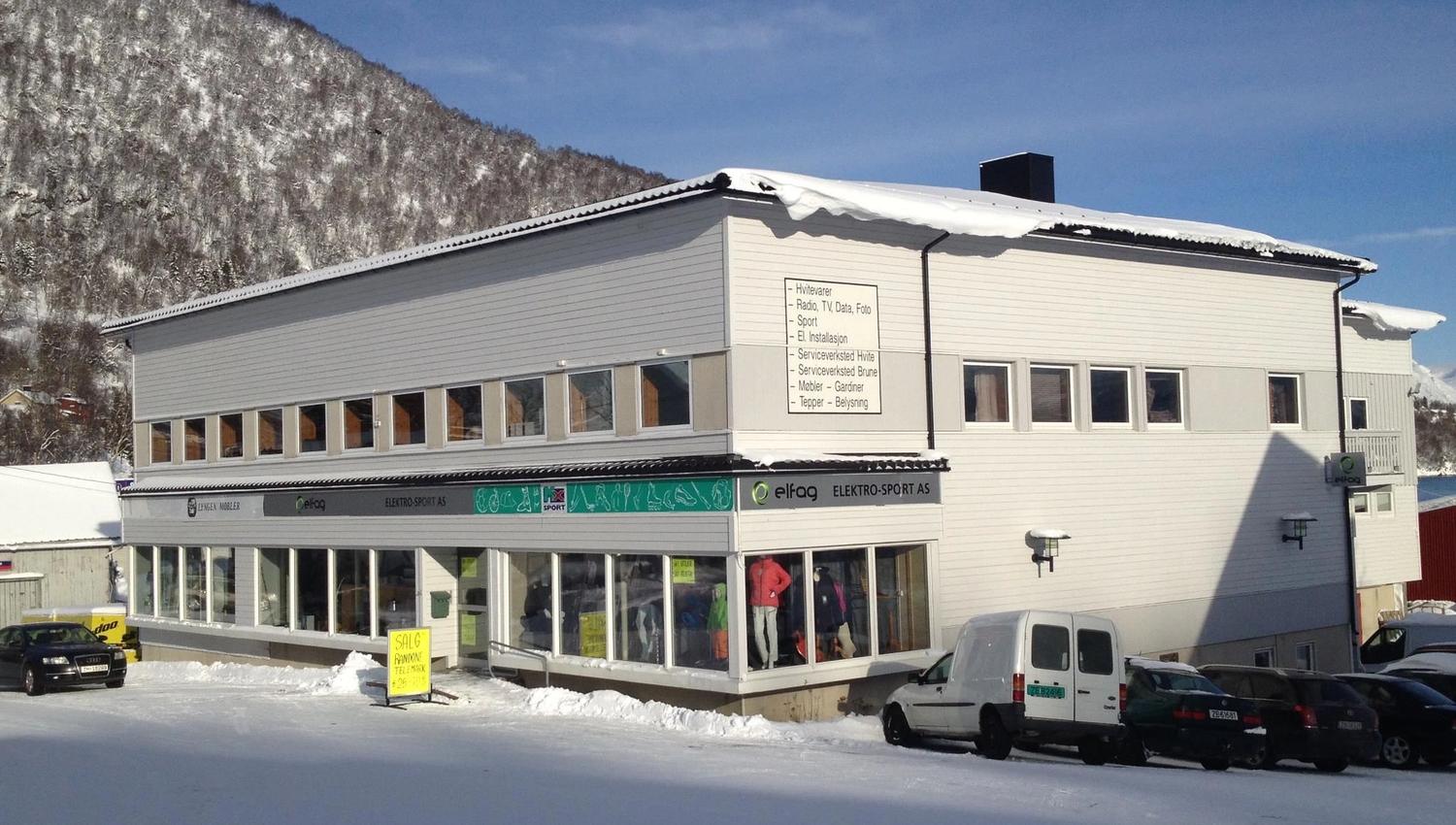 En hvit bygning med butikkvinduer i første etasjen. Tatt på en solrik vintersdag