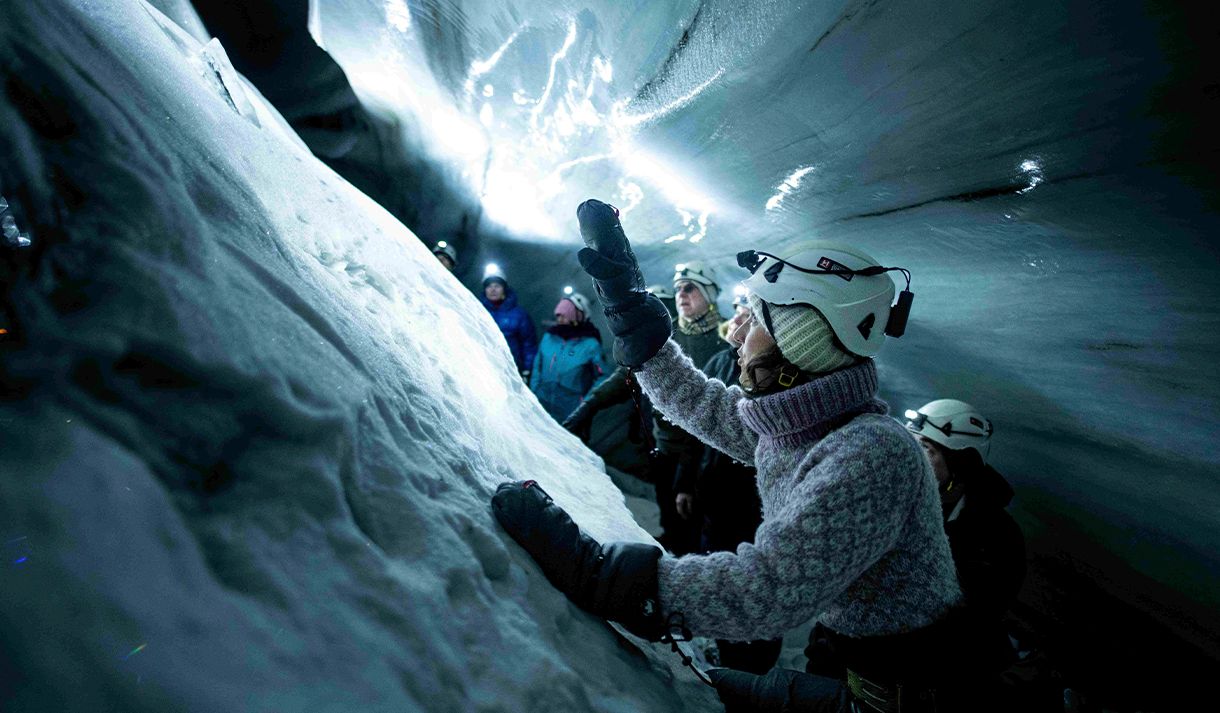 En guide med hodelykt og hjelm i forgrunnen som forteller gjester i bakgrunnen om isgrotten rundt de