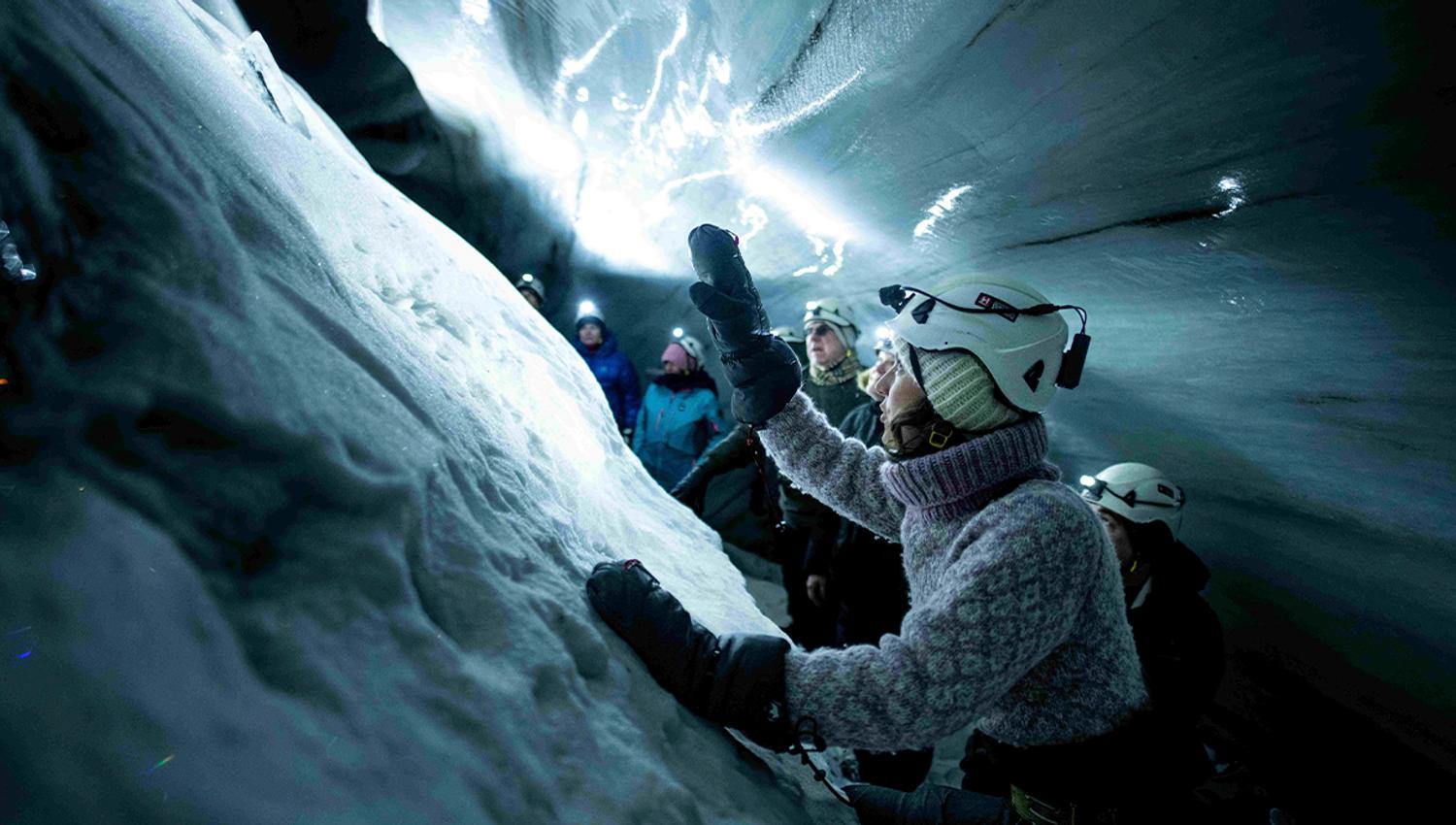 En guide med hodelykt og hjelm i forgrunnen som forteller gjester i bakgrunnen om isgrotten rundt de