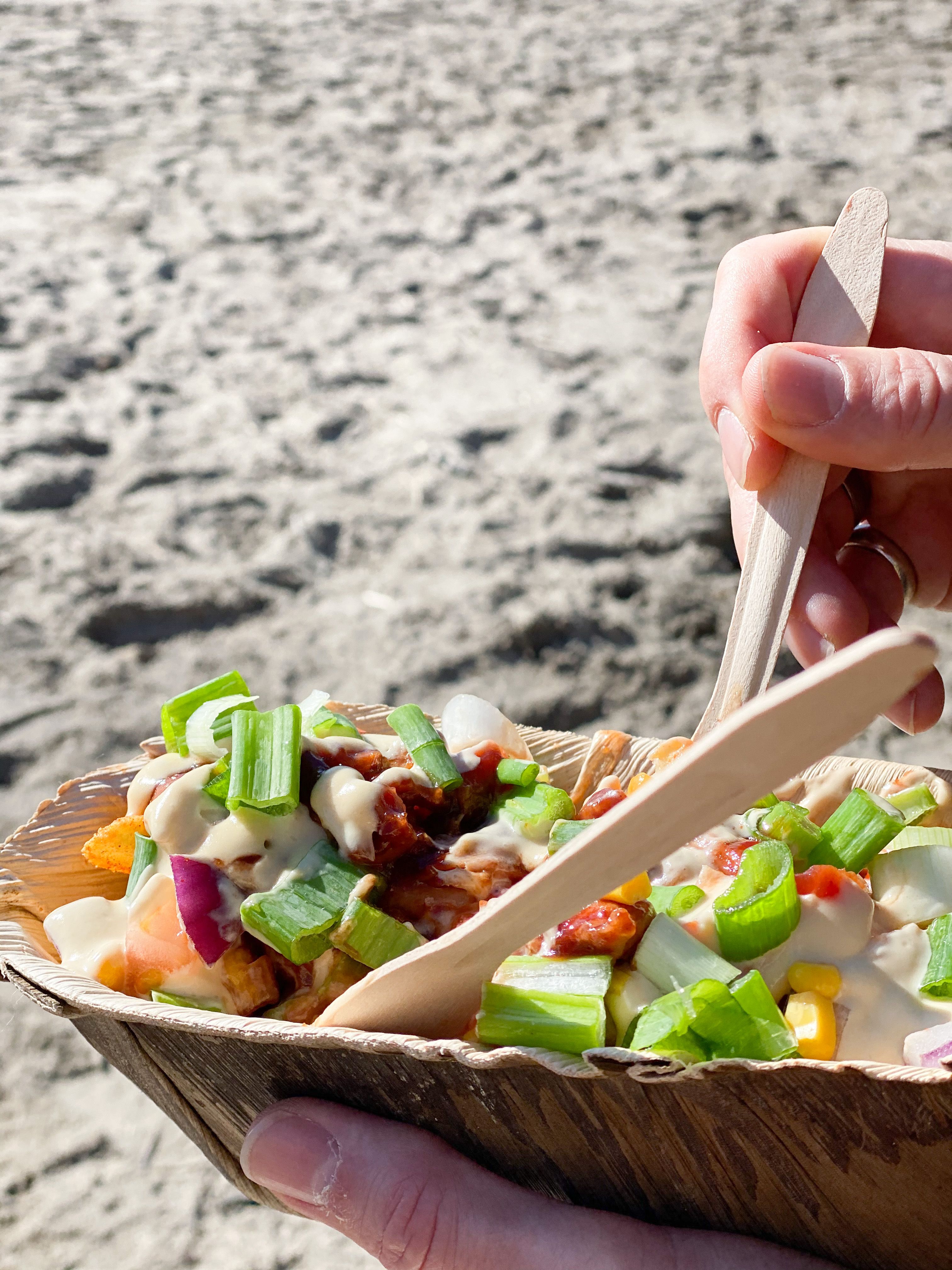 someone holding a plate with loaded fries. a beach in the background. photo.
