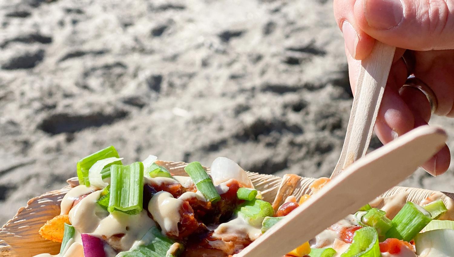 someone holding a plate with loaded fries. a beach in the background. photo.