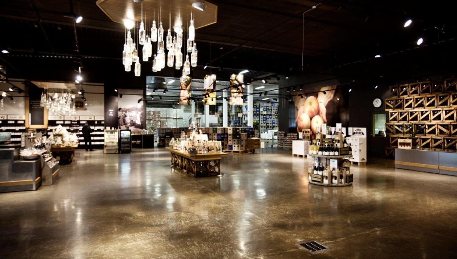 A modern store interior with shiny floors and bright lighting. Tables and shelves display bottles, jars, and local products. The ceiling lights are ma