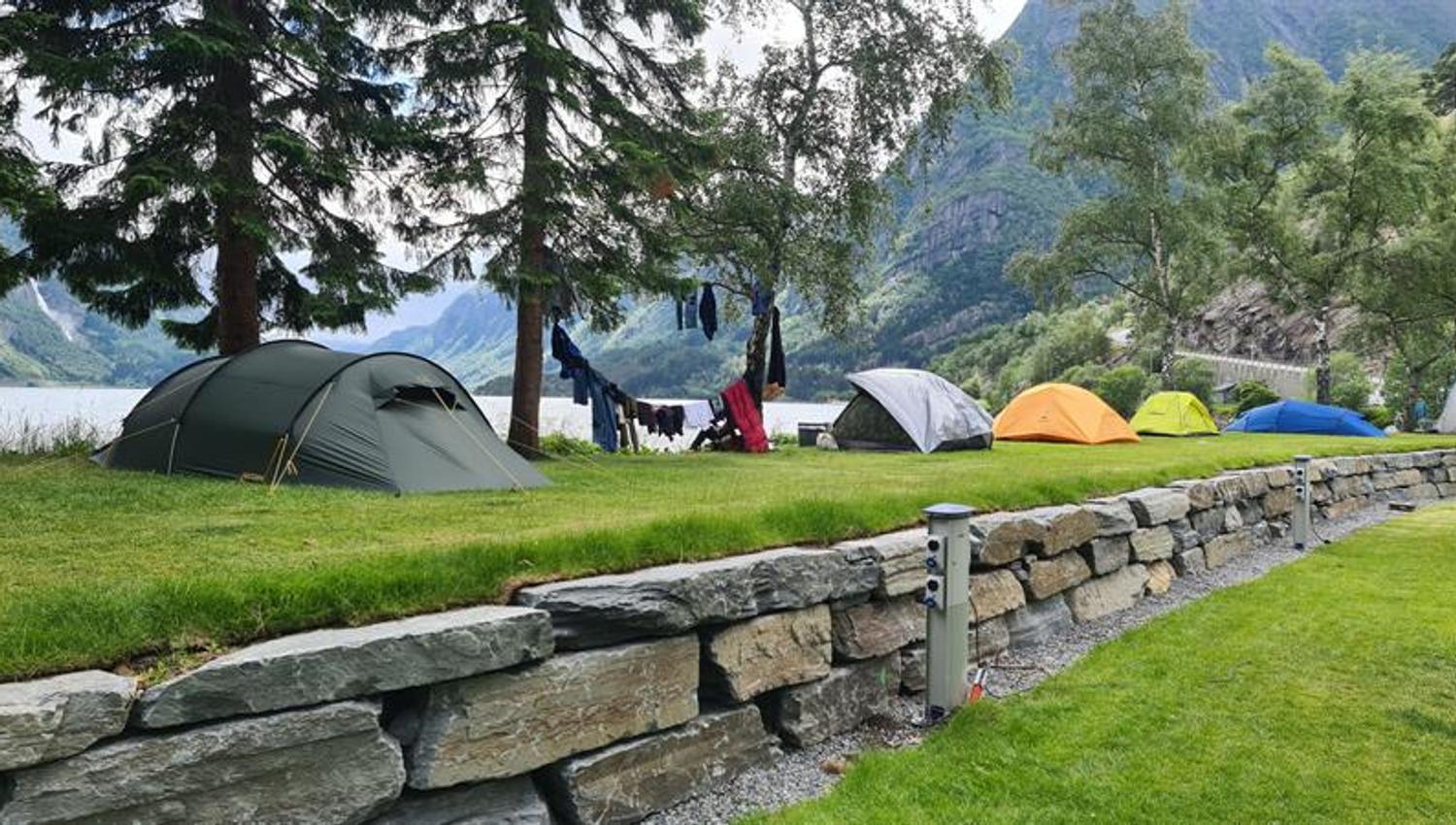 Tents on the grass by the water at Trolltunga Camping, surrounded by mountains and nature.