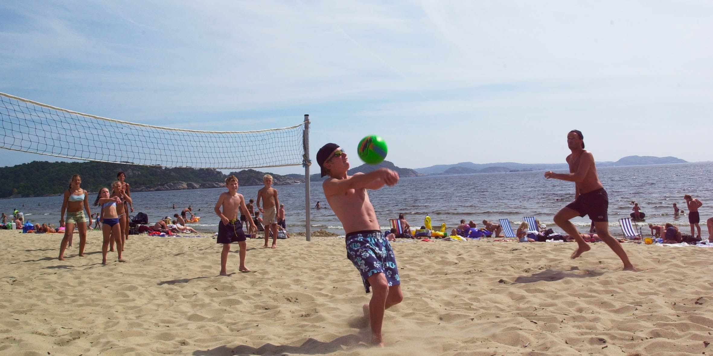 A group playing beach volleyball, where a guy is about to serve a green volleyball.