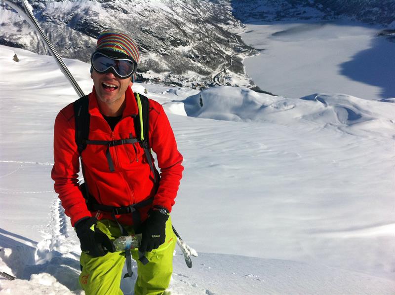 Fröhlicher Skifahrer auf einer Bergtour in Røldal mit Blick auf den Fjord und die Winterlandschaft.
