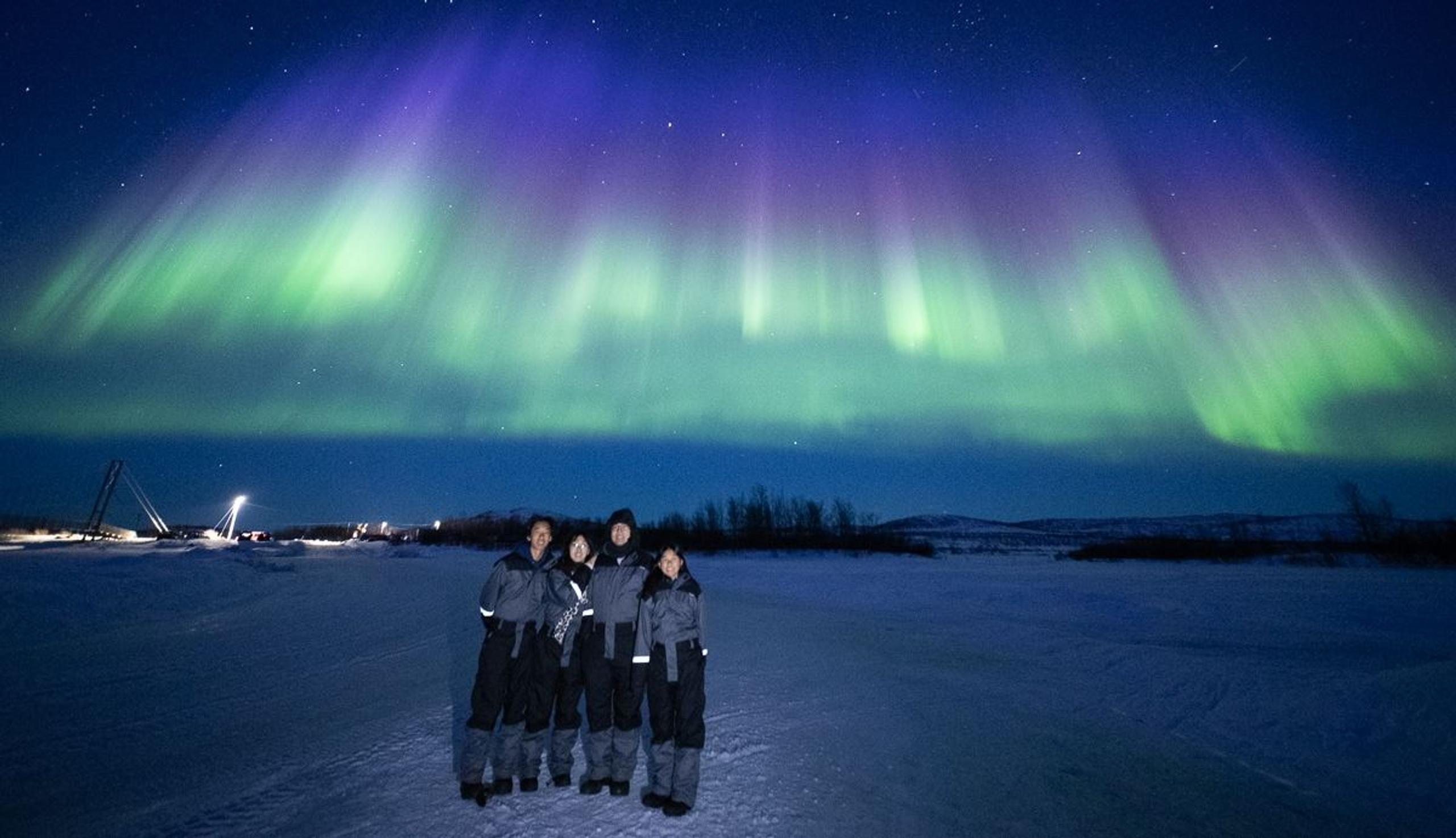 Guests stand together while the Aurora creates a blanket of blue, green and purple above them