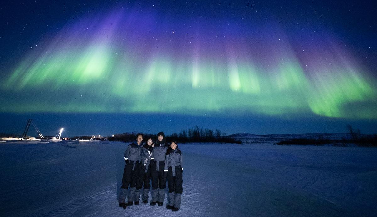 Guests stand together while the Aurora creates a blanket of blue, green and purple above them