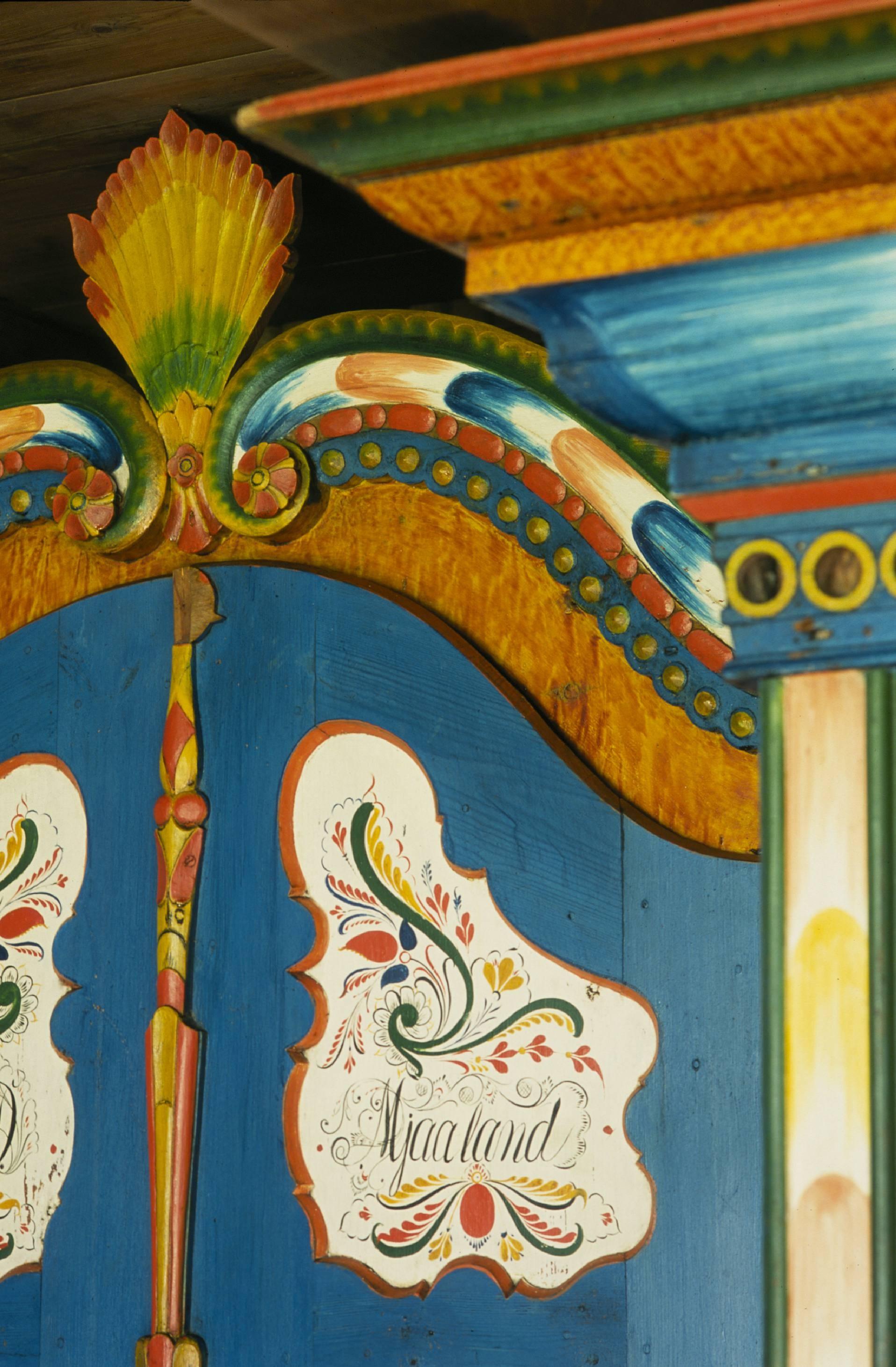 Blue cabinet with rosemaling and “Mjaaland” in cursive script