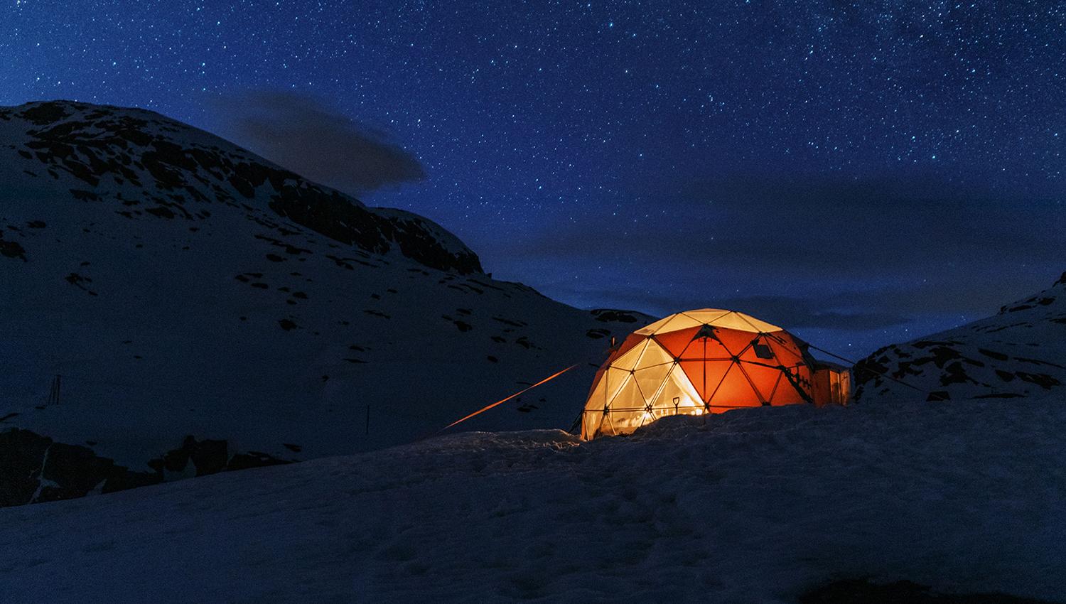 Illuminated geodome in a snowy mountain landscape under a starry winter sky near Trolltunga.