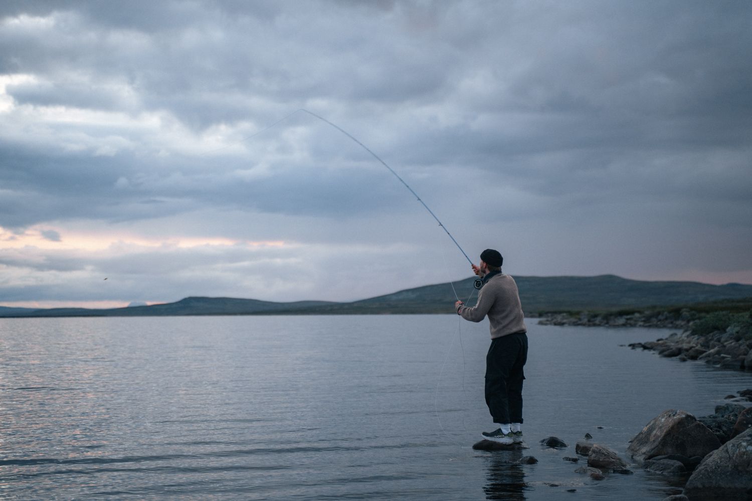 A man standing on a rock fishing in a mountain lake.