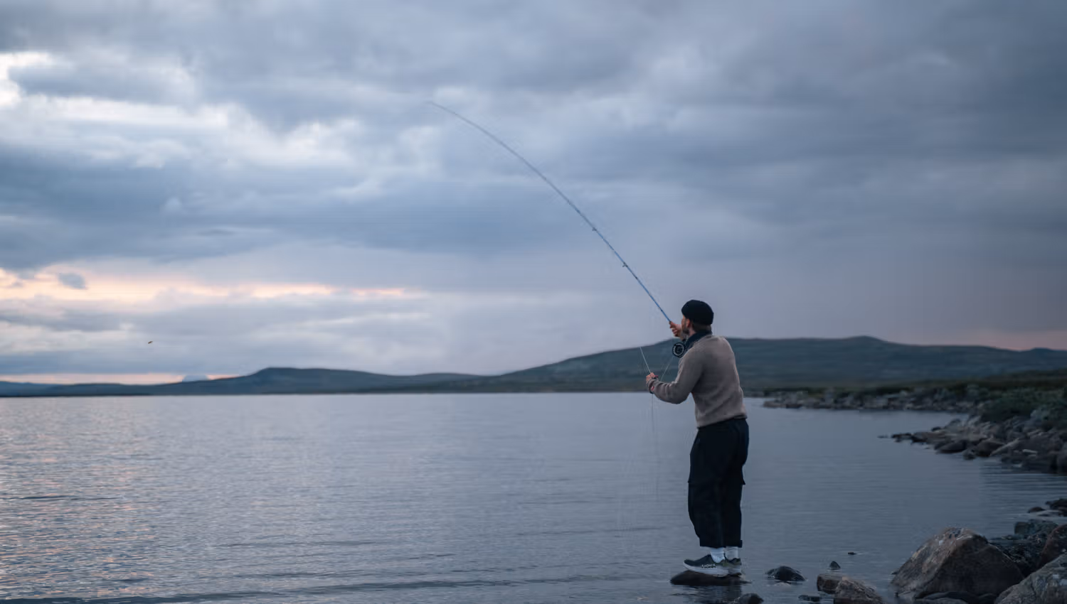 A man standing on a rock fishing in a mountain lake.